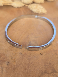 Bracelet jonc rigide argenté en acier inoxydable avec gravures décoratives.